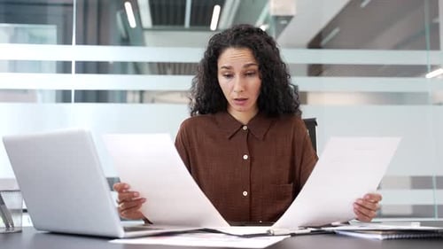 Empresaria confundida que tiene dificultades con el papeleo sentada en el lugar de trabajo en la oficina comercial.