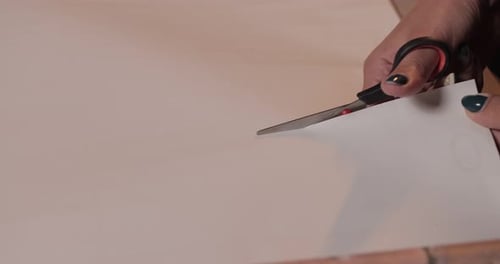 Close-up of young Caucasian woman's hands with black nails cutting self-adhesive wallpaper with scis