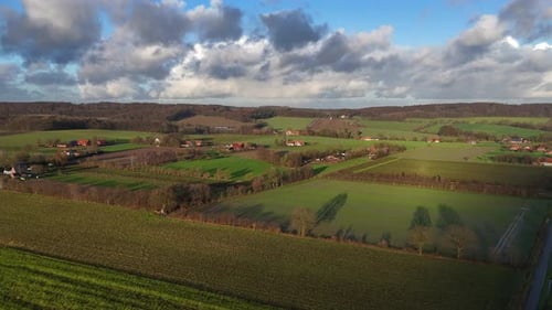 Aerial establishing shot of american farmsteads with green cultivated farm fields at sunset. Growing