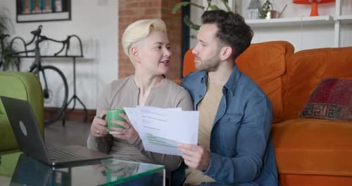 Couple Reviewing Documents Together at Home with Laptop