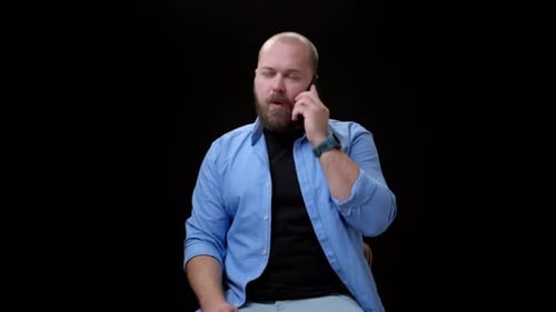 Bald Bearded Man in Blue Shirt on Black Background Answers Mobile Phone Call and Seriously Than