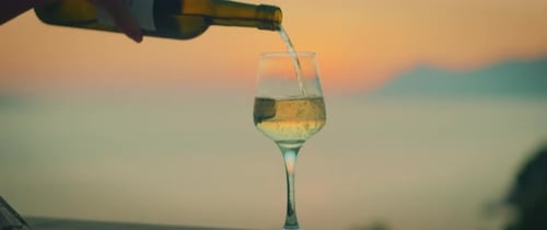 White wine being poured into glass during sunset with sea view in the background