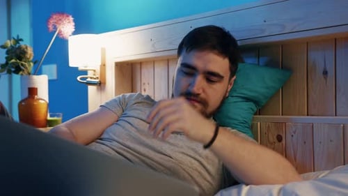 A Young Man is Relaxing Comfortably in Bed with a Laptop at Night Enjoying the Peaceful Atmosphere