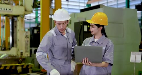 Asian adult male engineer points toward machine area while Asian adult female technician studies