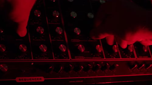 slow motion shot of a man turning knobs on a vintage synth, dark red and green mood