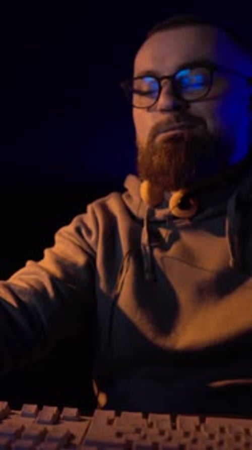 Vertical View of Man Working in Front of Desktop Computer Monitor From 1980's in Dark Room