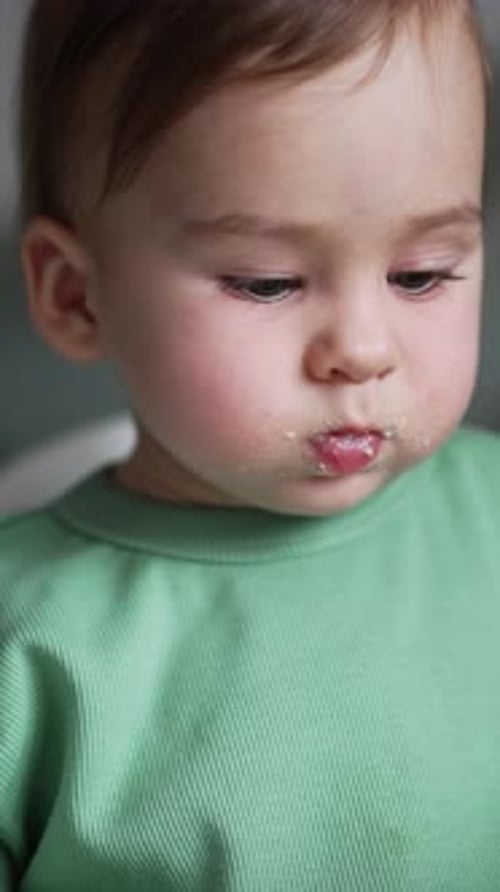 Um lindo bebê com comida em volta da boca está sentado na mesa de alimentação.