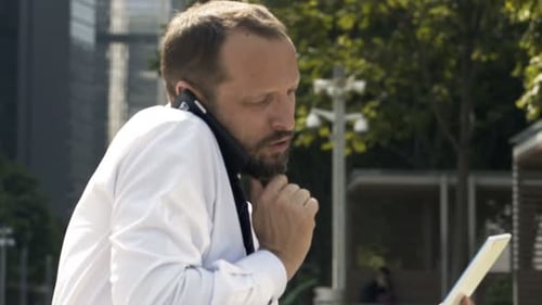 Young Businessman with Tablet Talking on Cellphone Sitting in City 30s