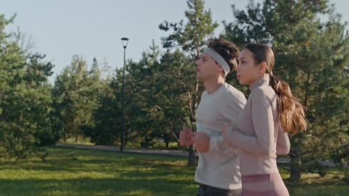 Young Active Couple Jogging Together in Public Park with Green Lawns