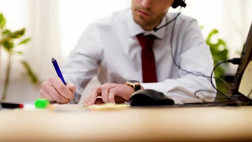 Businessman office worker taking note with pen while talking in video conference using headphone in