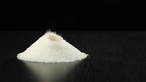 Cube of brown sugar is thrown into a heap of white sugar with splashes.