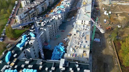 Flying over construction site. Top view of yellow tower cranes mounted on crane rails. A foreman in