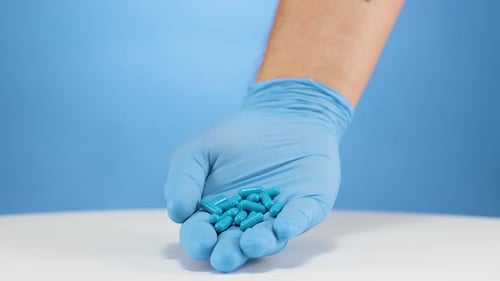 Médecin des mains tenant des pilules bleues dans des gants de protection en nitrile