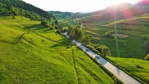 A Road Passes Hills Covered with Spruce Forests and Meadows Against a Cloudy Sky