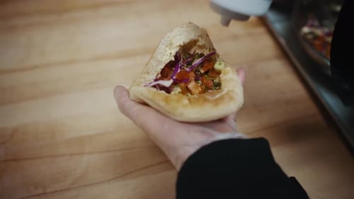 Pita Being Filled with Sauce and Vegetables