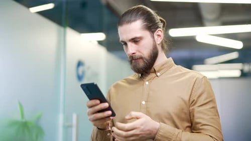 Happy excited businessman received great news on mobile phone standing in modern business office.