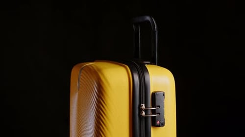 Yellow travel suitcase on black background rotating on stand close-up