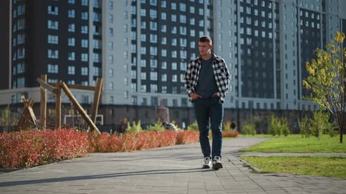 White Boy Walking Hands in Pockets Near People in Blur Background on Urban Path