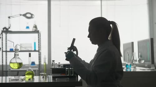 Side View of a Dark Silhouette of a Female Scientist Looking Under a Microscope Doing an Analysis of