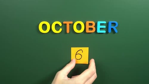 Hand sticking a sticker 6 October calendar day on school board. 6 date of October. Sixth day
