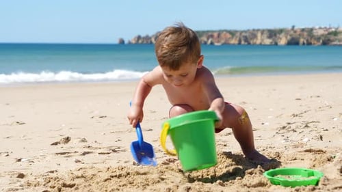 Cute Little Boy Playing with Bucket and Shovel in Sand at Sunny Beach