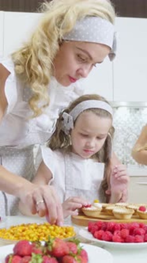 Cuisiner en famille dans une cuisine lumineuse en décorant des pâtisseries avec des fruits frais et de la crème