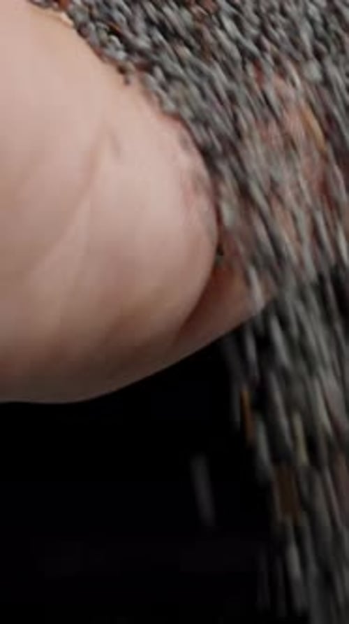 Vertical video. Poppy seeds falling from a man's hand, with a huge pile of seeds on the table. Slow