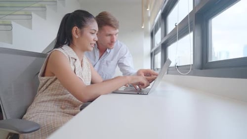 Caucasian man and Asian woman discuss about business work using laptop at table in office area