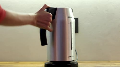 Person Putting Electric Kettle on Black Stand