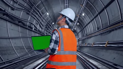 Back View Of Asian Male Engineer Working On A Green Screen Laptop In Subway Tunnel