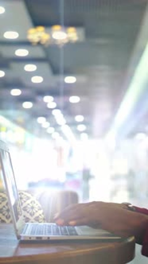Person Using Laptop at a Wooden Table in a Modern Cafe with Blurred Background Lights