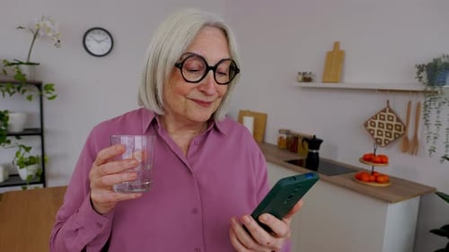 Smiling Senior Woman Using Smartphone in Kitchen