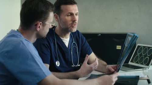 Side view of two male caucasian doctors discussing over medical X-ray scan on board. Shot with RED h