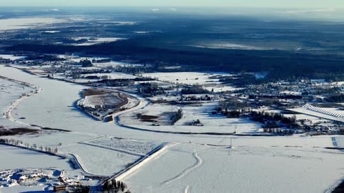 Stunning aerial view of a peaceful winter village in Northern Europe nestled by a frozen winding