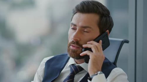 Portrait Of Company Employee Speaking Telephone Sitting In Office Wearing Elegant Suit. Confident...