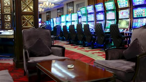 Slider shot of bright slot machines inside a casino display vivid screens with comfortable chairs