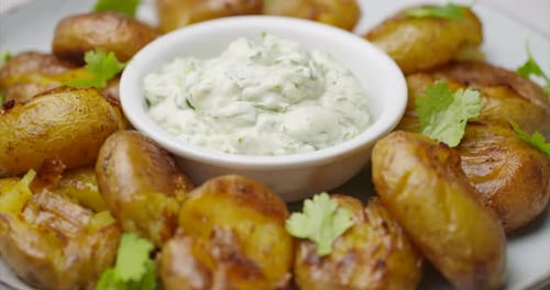 Sauteed potatoes on a white plate rotating. Potato with garlic dip. Healthy plant based vegan food.