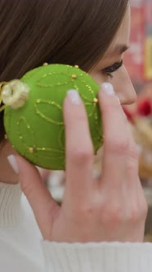 Closeup of Woman Checking Green Decorative Christmas Ball in Festive Decor Shop