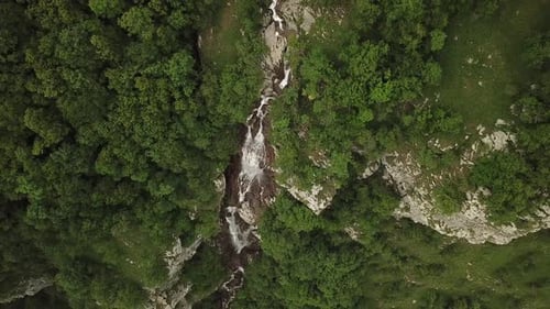 Eine Wasserkaskade steigt durch einen Wald herab. Felsen säumen die Wasserstraße. Die Aufnahme ist von oben aufgenommen.
