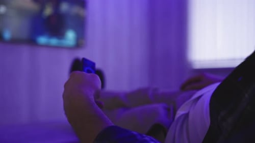 Person Reclines, Uses Remote Control in Dark Room