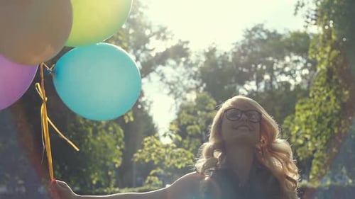 Happy Young Woman with Colorful Latex Balloons Gleefully Jumping for Joy in a Summer Park on a Sunny