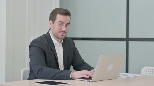 Smiling Man Types on Laptop, Gives Thumbs Up