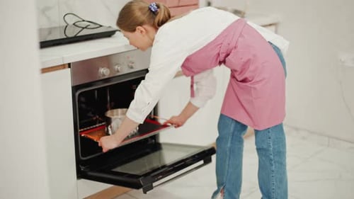 Confectioner woman in pink apron puts round metal ring with cheesecake in oven for baking