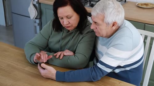 Senior Couple Enjoying Mobile Phone Together Indoors