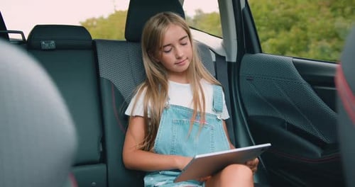 Adolescente assise sur le siège arrière de la voiture, utilise sa tablette PC et regarde dans la fenêtre pendant le voyage