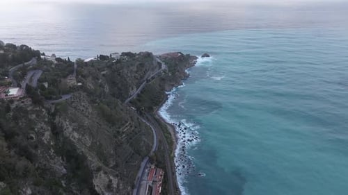 Eine Luftaufnahme eines Berghangs neben dem Meer, mit einer kurvenreichen Straße, die am Hang entlang verläuft.