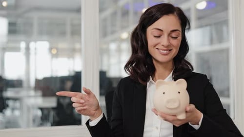 Businesswoman Holding Piggy Bank and Pointing to Blank Space in Office