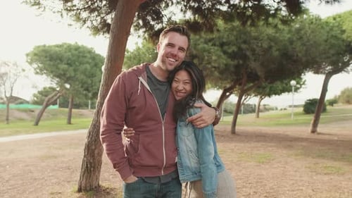 Laughing couple hugging each other while standing in the park