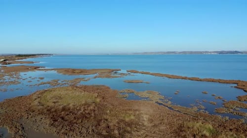 Peaceful calm lagoon with clear water bordered bu brown banks with dried grass and reeds, panoramic