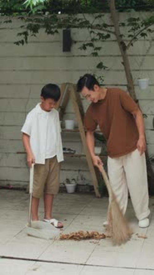 Father and Son Sweeping Leaves Together at Home